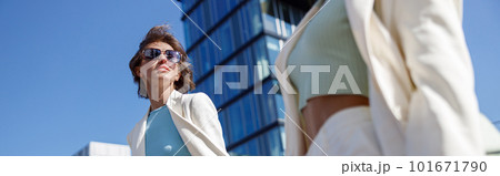 Two happy woman in trendy outfits laugh and walk outside on background of modern building 101671790
