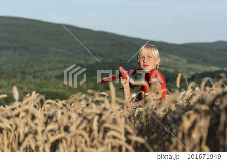 Blond boy holds model of an airplane stay on wheat field on hill background. Weekend countryside. Child dreams about traveling. Blond boy holds model of an airplane stay on wheat field on hill background. Weekend countryside. Child dreams about traveling. 101671949