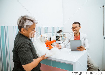 a male vet bring a tablet while meeting a cat and it's owner a male vet bring a tablet while meeting a cat and it's owner 101673134