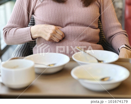 たくさんのお皿を前にしてお腹の肉をつまむ女性 101674179