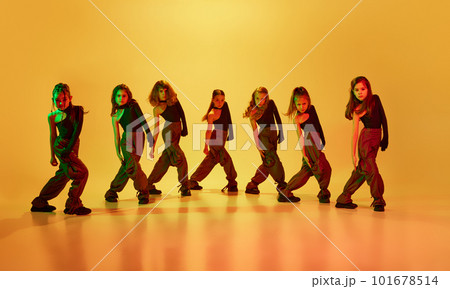 Little artistic girls, children in sport style clothes dancing hip-hop against yellow studio background in neon light. Beauty of movements 101678514