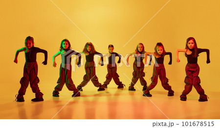 Group of artistic, little dancers, girls, children in stylish sportive clothes dancing hip-hop against yellow studio background in neon light 101678515