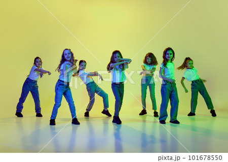 Dynamic image of little girls, children dancing against green studio background in neon light. Casual clothes. Hip-hop style 101678550