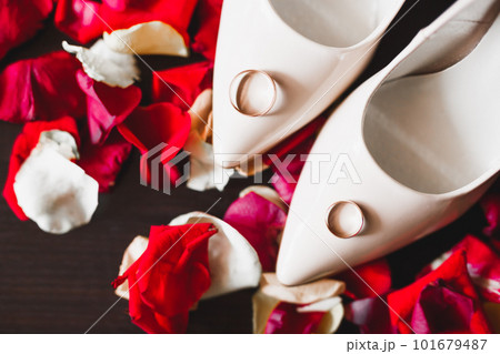 Beautiful toned picture with wedding rings on wedding shoes against the background of flowers 101679487