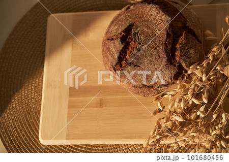 Top view of freshly baked rye bread on a yeast-free starter and on mixture of whole grain, rye and wheat flour. It lies on cut board next to a dried flower with grains. Selective focus, sun.Copy space 101680456