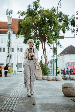 female traveller with hijab looking at her phone while walking female traveller with hijab looking at her phone while walking 101681360