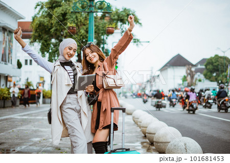 two happy travellers raising her hands while standing together at the sidewalk 101681453