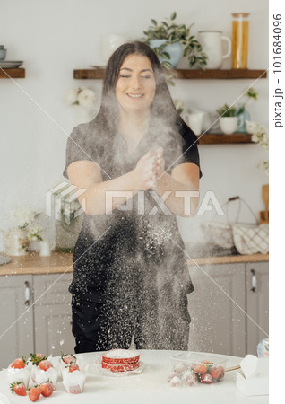 Woman baker clapping and sprinkling white flour over dough on kitchen background 101684096