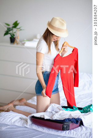 Beautiful young woman looking carefree and positive while packing her suitcase 101684207