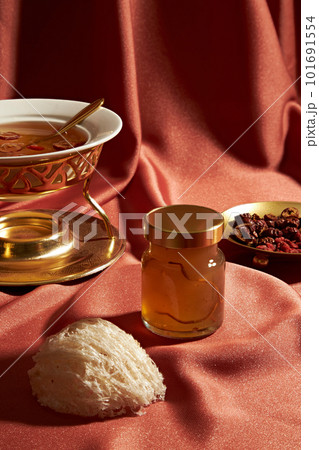 Front view of a bottle of bird nest unlabeled, raw bird nest and jujube, wolf berry, soup on a red soft fabric background. Mockup scene advertising bird nest products are distilled with herbs 101691554