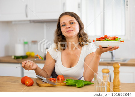 Young woman eating vegetable salad in kitchen 101692344