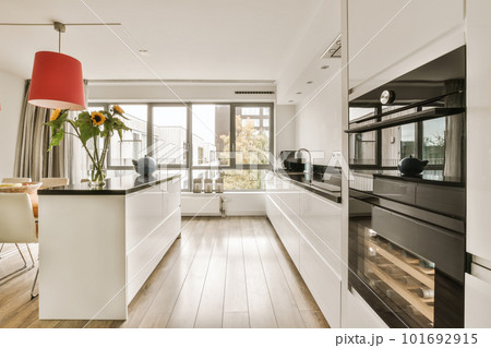 a modern kitchen with wood flooring and white cabinets in the center of the room is a red lamp hanging over the island 101692915