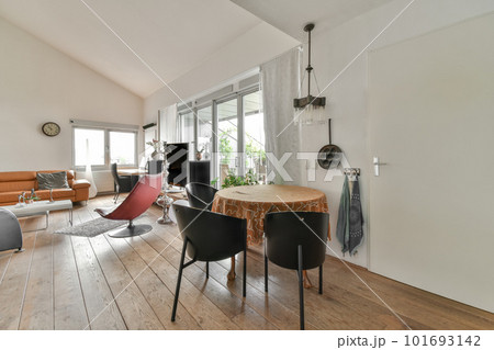 a living room with wood floors and white walls, including a round dining table surrounded by two black leather chairs 101693142