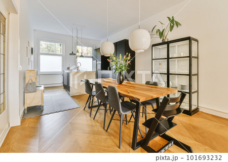 a dining room with wood flooring and white walls there is a wooden table, black chairs and a plant on the wall a dining room with wood flooring and white walls there is a wooden table, black chairs and a plant on the wall 101693232