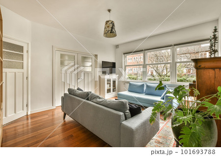 a living room with wood flooring and a blue couch in the center of the room is a large window a living room with wood flooring and a blue couch in the center of the room is a large window 101693788