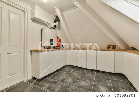 a small kitchen in a loft style space with tile flooring and white cupboards on either side, there is an open door a small kitchen in a loft style space with tile flooring and white cupboards on either side, there is an open door 101693801