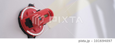 Red construction laser level fixed on white wall 101694897