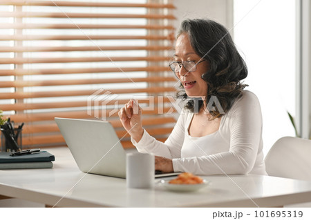 Attractive senior woman in glasses watching online webinar on laptop during remote working from home Attractive senior woman in glasses watching online webinar on laptop during remote working from home 101695319