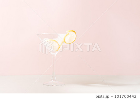 Glass goblet with ice and lime slices against pink background 101700442