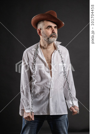 Stern serious elderly man in a white shirt, in a cowboy hat and with a metal chain in his hands Stern serious elderly man in a white shirt, in a cowboy hat and with a metal chain in his hands 101704458