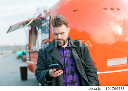 Portrait of handsome young man with smartphone standing in front of food truck - food delivery and restaurant app Portrait of handsome young man with smartphone standing in front of food truck - food delivery and restaurant app 101706583