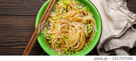 Asian noodles soup in green rustic ceramic bowl with wooden chopsticks top view on dark wooden background. Lo mein noodles with broth, green onion Asian noodles soup in green rustic ceramic bowl with wooden chopsticks top view on dark wooden background. Lo mein noodles with broth, green onion 101707588