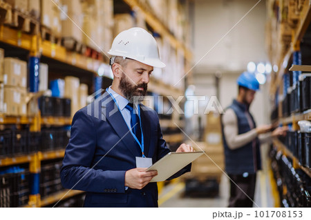 Manager in suit controlling goods in a warehouse. 101708153