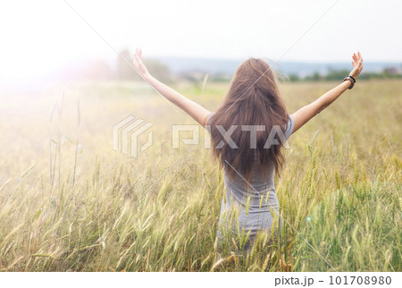 Young woman with long brown hair standing in wheat field raising 101708980