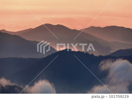 Wide panorama, fantastic view of covered with morning mist green Carpathian mountains at sunset on bright clear orange sky copy space background. Beauty of nature, tourism and traveling concept. 101709229