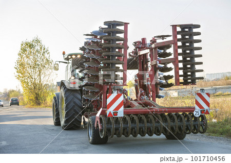 Tractor combine with disc harrows driving along rural road on sunny day. Agricultural machinery and farming concept. 101710456