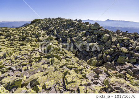 Stack of stones covered with moss on top of a mountain on mountains background. Concept of balance and harmony. Stack of zen rocks. Wild nature and geology detail. Stack of stones covered with moss on top of a mountain on mountains background. Concept of balance and harmony. Stack of zen rocks. Wild nature and geology detail. 101710576