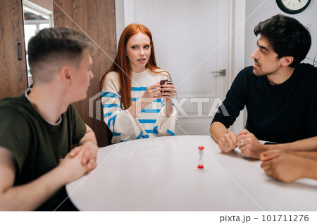 Happy multiethnic friends having play cards games for time, enjoying board games activity for entertainment at home. Cheerful diverse people playing UNO board game sitting at table. 101711276