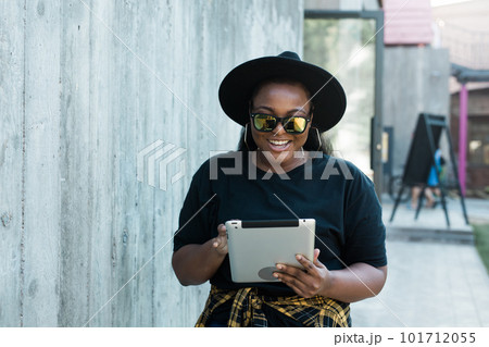 Portrait of beautiful curly African American girl standing urban background and holding digital tablet. charming young female with a tablet pc Portrait of beautiful curly African American girl standing urban background and holding digital tablet. charming young female with a tablet pc 101712055