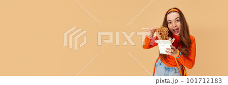Banner with young adorable girl holding box with food and eating noodles with hunger face on ginger studio background. Junk, unhealthy food 101712183