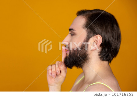 Side view of bearded transsexual person holding finger near lips making silence gesture keeps secret Side view of bearded transsexual person holding finger near lips making silence gesture keeps secret 101716255