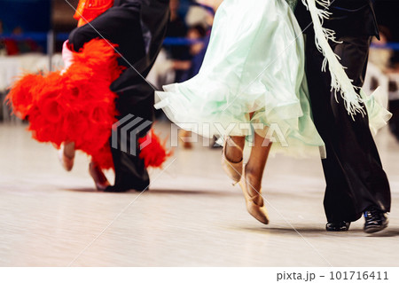 couples dancing viennese waltz in competitive ballroom dancesport, woman is wearing purple and red dress, man on black tail suit 101716411