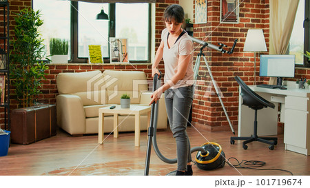 Young woman sweeping dirt with mop in living room, mopping wooden floors and cleaning apartment. Casual female person washing tiles with cleaner, being focused on housework or chores. Young woman sweeping dirt with mop in living room, mopping wooden floors and cleaning apartment. Casual female person washing tiles with cleaner, being focused on housework or chores. 101719674