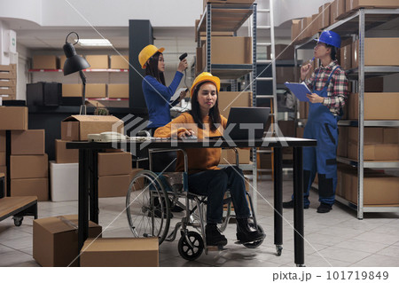 Warehouse employee doing office work in disability friendly workplace. Young asian woman postal service worker in wheelchair checking products stock logistics on laptop in storehouse Warehouse employee doing office work in disability friendly workplace. Young asian woman postal service worker in wheelchair checking products stock logistics on laptop in storehouse 101719849