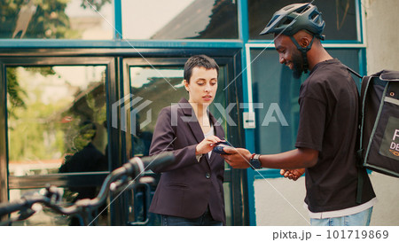 Female client paying for food delivery order with credit card, woman using pos terminal contactless payment for fastfood meal. Delivery service courier with backpack delivering package. Handheld shot. Female client paying for food delivery order with credit card, woman using pos terminal contactless payment for fastfood meal. Delivery service courier with backpack delivering package. Handheld shot. 101719869