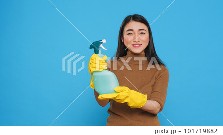 Smiling asian maid wearing protective gloves while showing chemical detergent spray in front of camera, promoting cleaning product. Professional housekepper worked hard to maintain a clean home Smiling asian maid wearing protective gloves while showing chemical detergent spray in front of camera, promoting cleaning product. Professional housekepper worked hard to maintain a clean home 101719882