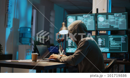 Masked data thief hacking computer network at night, working on laptop and multiple monitors to steal IT information. Hacker with hidden identity, server security breach. Handheld shot. Masked data thief hacking computer network at night, working on laptop and multiple monitors to steal IT information. Hacker with hidden identity, server security breach. Handheld shot. 101719886
