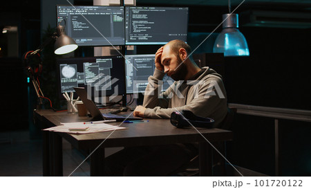 Young man feeling tired and working on programming code, typing database information and html script on laptop. Adult falling asleep at office, being exhausted using terminal window. Handheld shot. 101720122