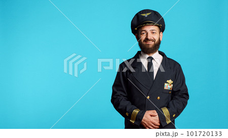 Male plane captain wearing airline uniform and posing in studio, having professional occupation. Young adult working as pilot to fly airplane, being cheerful and positive on camera. 101720133