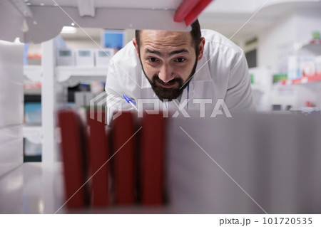 Pharmacist looking at shelves full with pills packages doing inventory writing medication name on papers, working in pharmacy. Drugstore worker is responsible for reviewing orders to ensure accuracy. Pharmacist looking at shelves full with pills packages doing inventory writing medication name on papers, working in pharmacy. Drugstore worker is responsible for reviewing orders to ensure accuracy. 101720535