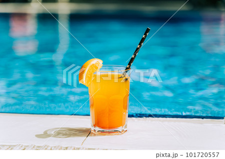 Tropical sparkling cocktail by the pool. The shot of glass with orange lemonade fruit cocktail standing near the poolside. Summer alcohol free drink by the hotel pool. Hello summer holiday vacation 101720557