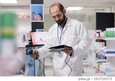 Drugstore worker checking medication information on tablet computer while scanning vitamins and supplements with store scanner in pharmacy. Pharmacist doing pills inventory, health care concept 101720573
