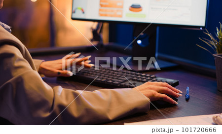 Office worker typing financial information on computer, working with research plan and economy diagrams at night. Young entrepreneur using analytics to help increase profit for development. 101720666