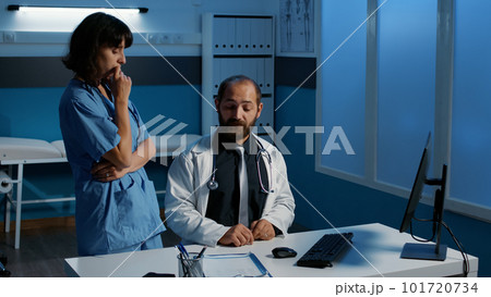 Medical staff analysing patient illness expertise report discussing health care treatment, working late at night in hospital office during checkup visit. Medicine service and concept 101720734