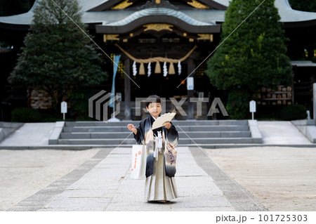 和服姿で七五三のお宮参りに来た5歳児が扇子を胸の前で広げ神社の社殿をバックににこやかに立っているとこ 和服姿で七五三のお宮参りに来た5歳児が扇子を胸の前で広げ神社の社殿をバックににこやかに立っているとこ 101725303