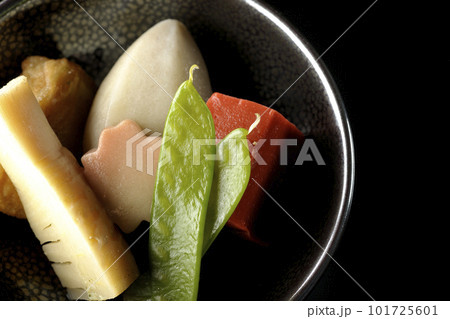 筍や里芋、生麩、サヤエンドウ等が入っている煮物を黒背景で俯瞰撮影 101725601
